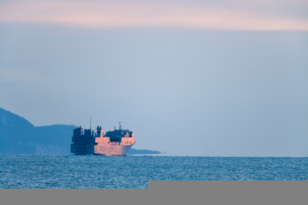 Photograph of a military ship on dark blue water, during a sunrise, exiting Kachemak Bay in Alaska