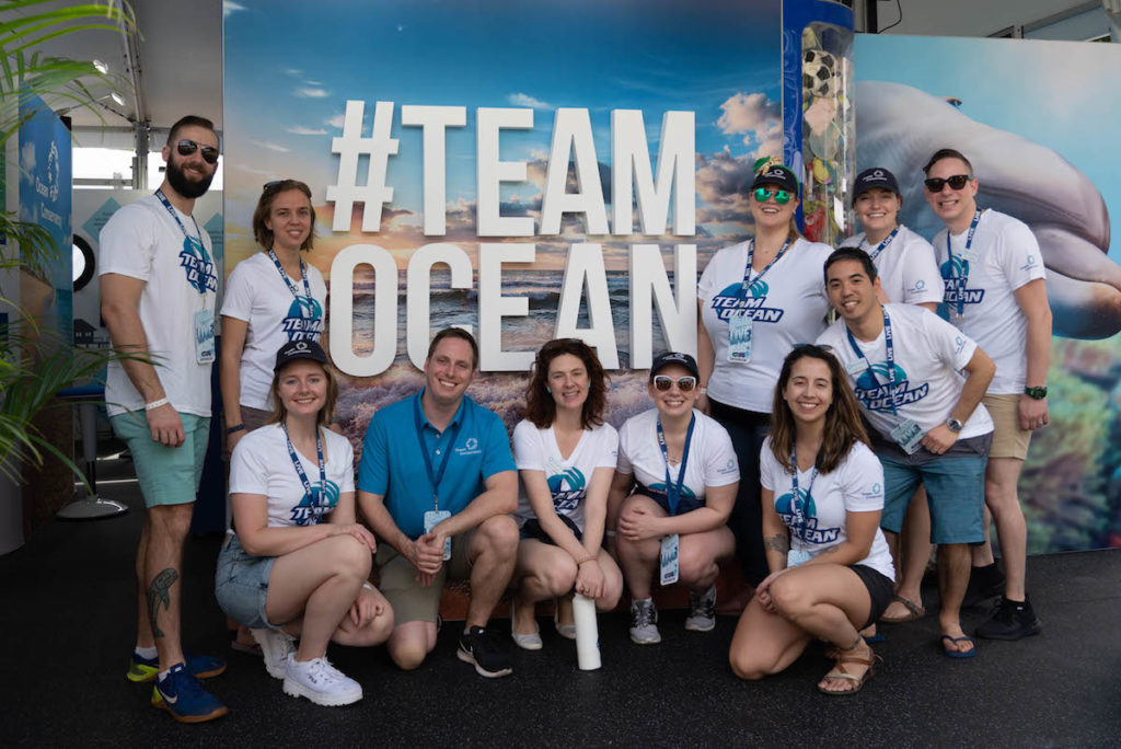 A group of Ocean Conservancy employees wearing white t-shirts that say "TEAM OCEAN" in blue letters at the Super Bowl LIV booth in Miami.